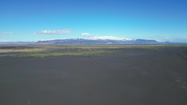 Survol d'une plage noire de sable noire avec une plaine et un glacier islandais en fond