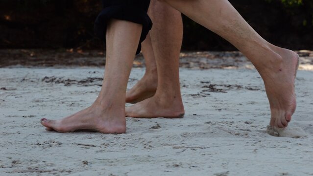 Male and female legs of pair walking on sandy beach. Bare feet of couple stepping along sand shore at sunny day. Lovers spending time together at resort. Concept of summer vacation or holiday