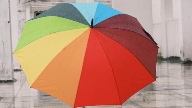 Colorful rainbow umbrella open in rainy street of Paris, France &mdash; vibrant multi-hued canopy against