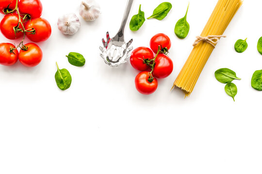 Cooking italian pasta. Spaghetti, tomatoes, garlic, basil and cookware on white background top view copy space