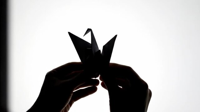 Silhouettes of Hands Creating Origami Shapes Against Bright Backgrounds.