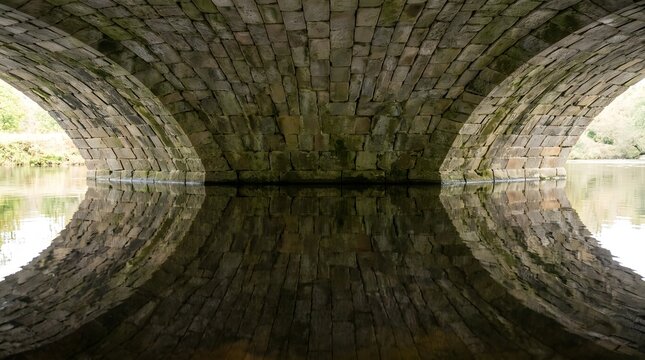 View through ancient stone bridge arch tunnel with weathered texture and natural light 
