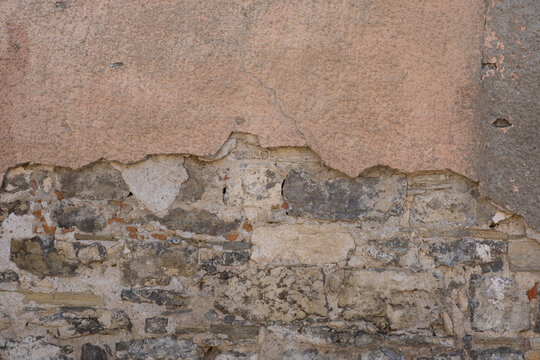 Weathered background with cracked wall and exposed stones in a building located in an old town during day
