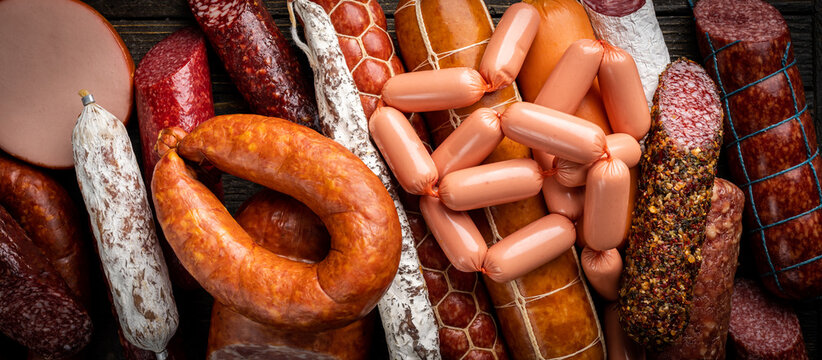 Set of different types of sausages, salami and smoked meat with basil and spices on wooden background. Top view.