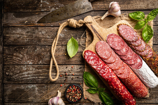 Set of different types of sausages, salami and smoked meat with basil and spices on wooden background. Top view.