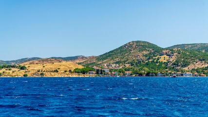 Fototapeta premium Izmir, Turkey - June 21, 2026: Scenic nature view near Foça, featuring Mediterranean vegetation, rocky coastline, green hills, blue Aegean Sea, calm water, and natural coastal landscape.