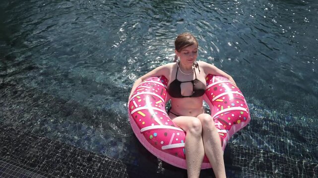 Beautiful woman floating in swimming pool on inflatable donut ring