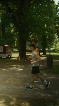 Two men are running through a lush green park on a bright sunny day. They share an active and healthy outdoor workout experience.