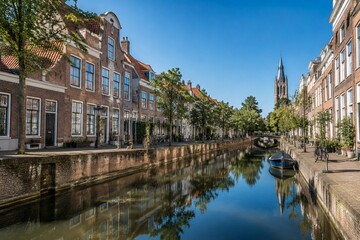 Obraz premium Serene canal in Delft with red brick houses and calm water reflection.