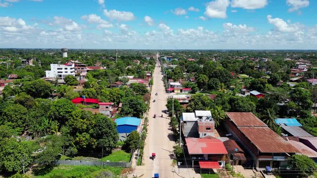 Cinematic aerial drone flight tracking a long, unpaved avenue in Yarinacocha, Pucallpa, showing light traffic of motorcycles and mototaxis moving toward the green Amazon horizon.