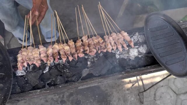 Chicken satay skewers grilling over hot charcoal with smoky street food atmosphere, close-up barbecue cooking process, and authentic Indonesian cuisine footage.