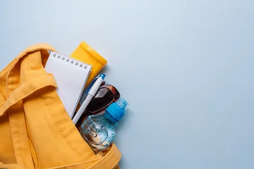 Yellow tote bag with water bottle, sunglasses, notepad and pen on blue background. © Anastassiya 