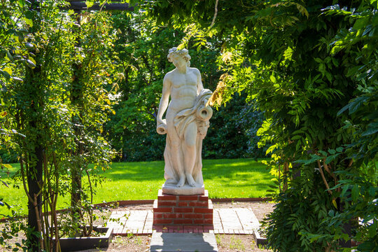 Classical marble garden statue on brick pedestal surrounded by lush trees at Kiviks Hotell
