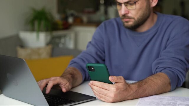 Man entering information from smartphone into laptop