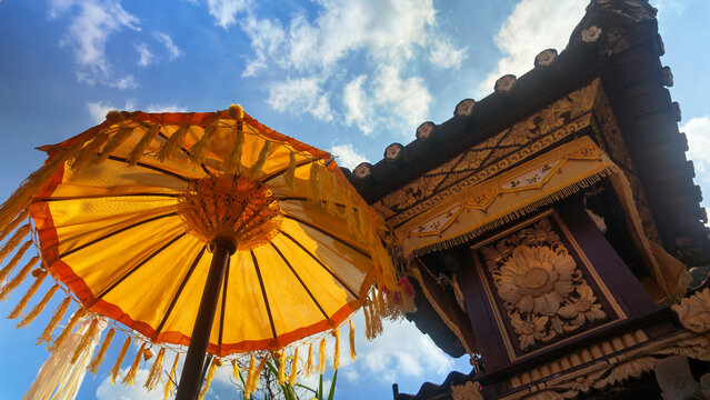 Traditional Balinese yellow ceremonial umbrella and temple shrine carving under blue sky