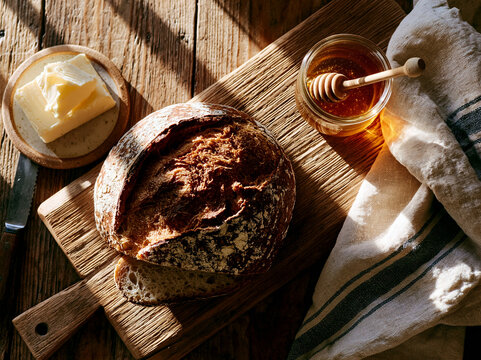 Rustic Sourdough Bread Loaf on Wooden Cutting Board with Butter and Honey