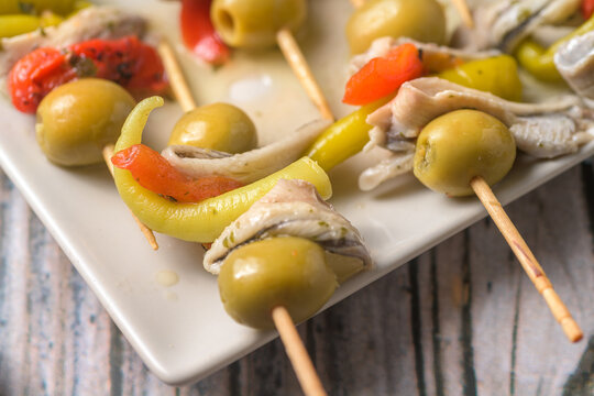 Traditional Spanish gildas skewers with green olives anchovies and hot peppers served on a plate with white wine on a rustic wooden table