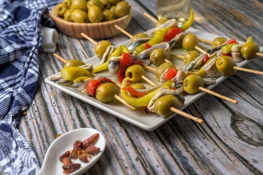 Traditional Spanish gildas skewers with green olives anchovies and hot peppers served on a plate with white wine on a rustic wooden table