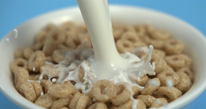 Milk pouring into wheat cereal rings in bowl with splash in super slow motion