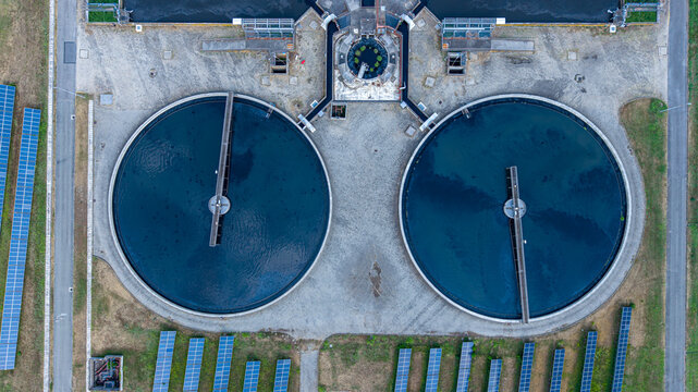 Aerial view of a wastewater treatment plant with two large circular sedimentation tanks and rows of solar panels in Settimo Torinese, Piedmont, Italy.