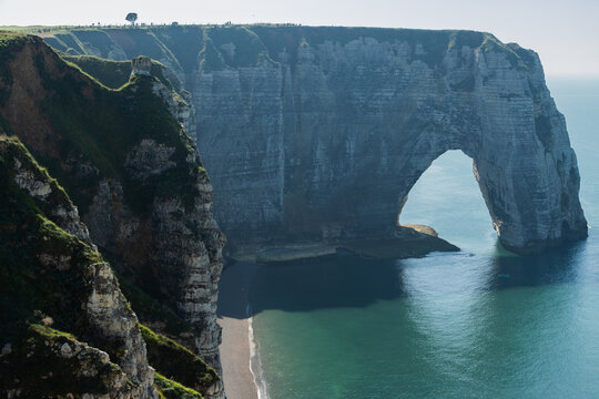 Dramatic view of the famous natural chalk arch and rugged coastline at &Eacute;tretat, Normandy, France. Bright sunny day with turquoise sea and pebble beach.