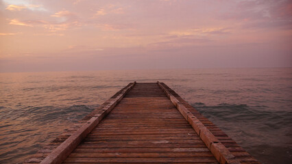 Close-up of a rustic wooden groyne extending into calm ocean water under a pastel morning sky © Nelia