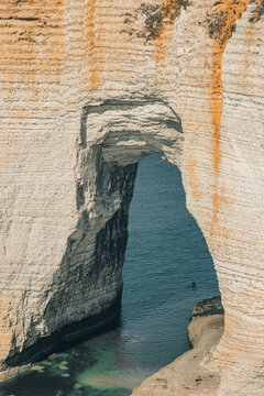 Close-up view looking through the massive Aval natural chalk arch into the blue sea in &Eacute;tretat, Normandy, France. Two small boats visible on the water.