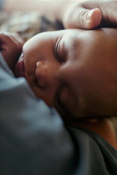Vertical shot of infant sleeping against mother while hand resting on head, conveying maternal care and bonding. Useful for parenting, maternity leave, childcare, family support campaigns