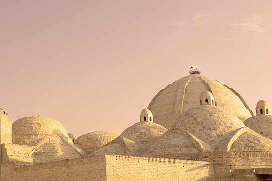 Brick domes of Toqi Zargaron covered bazaar in Bukhara with a stork nest on top against a warm sunset sky. Ideal for travel publications, cultural heritage projects, and Central Asian tourism.