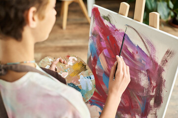 A young woman in a relaxed setting focuses on painting with vibrant colors at home, expressing her creativity. © LIGHTFIELD STUDIOS