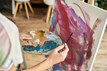 A young woman with short hair paints on a canvas, embracing her artistic hobby in a cozy environment. © LIGHTFIELD STUDIOS