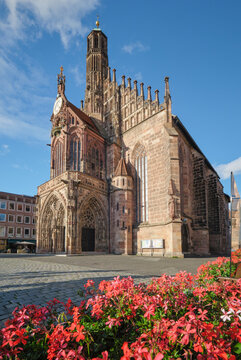 Frauenkirche church on Hauptmarkt in Nuremberg, Germany, seen above red flowers with Gothic stonework and old town square light