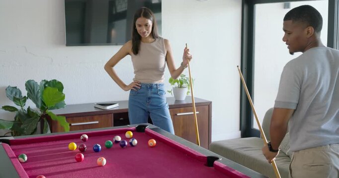 African American couple breaking rack on pool table at home, man guiding woman preparing shot