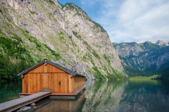 Scenic view of a rustic wooden boathouse and dock on the emerald waters of Obersee lake in Berchtesgaden, Bavaria, Germany.