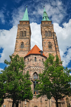 Front view of St Sebaldus Church in Nuremberg, Germany, with twin church towers, red roof detail and trees below
