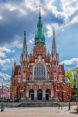 Fototapeta premium Close view of Saint Joseph Church in Podgorze, Krakow, Poland, showing red brick Gothic architecture, tall steeples, church facade, blue sky, and no people