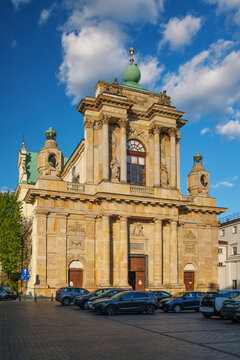 Street view of the Carmelite Church facade on Krakowskie Przedmiescie in Warsaw with baroque architecture, parked cars, traffic sign, and spring clouds