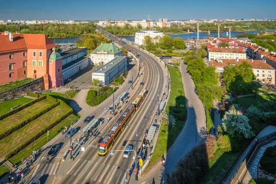 Elevated view over Warsaw W-Z Route with tram lane, road traffic, Royal Castle gardens, red rooftops, and Vistula-side city blocks