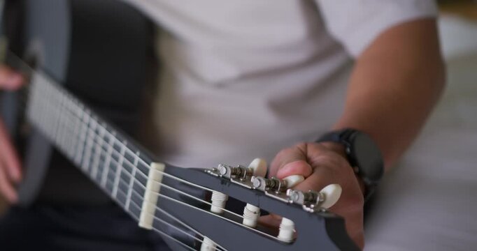 Right hand is turning white tuning peg after hearing low string pitch, tuning guitar on couch