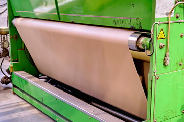 Close up view of continuous paper web feeding into a corrugator production machine line in a packaging plant. © Констянтин Батыльчук