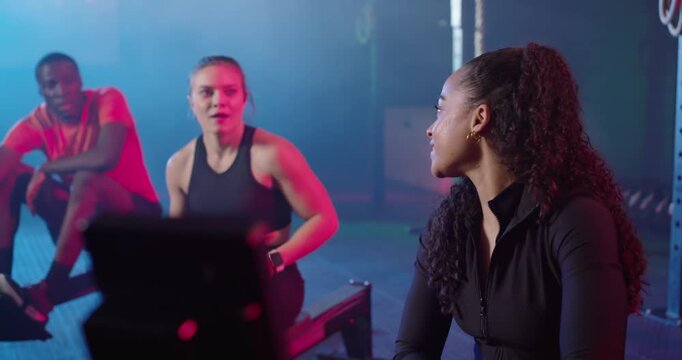 Diverse group starting set on rowers in gym, woman tracking pace on watch, fist-bumping, copy space