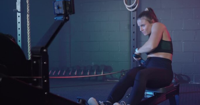 Female athlete wearing black top pulling handle on rower, monitor showing interval initiating power