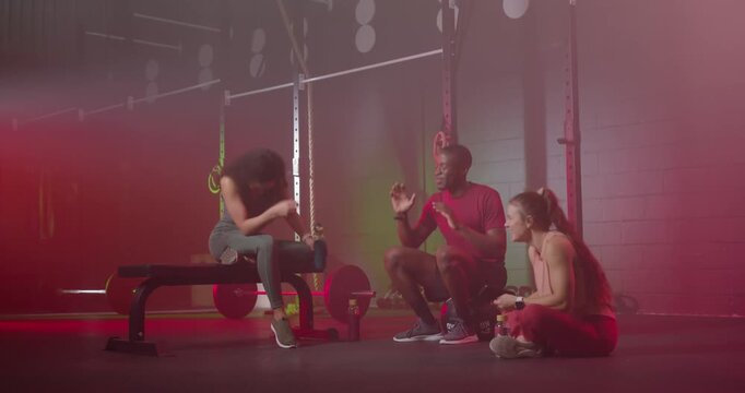 Diverse friends laughing, showing phone screen and gesturing beside weight bench during cooldown