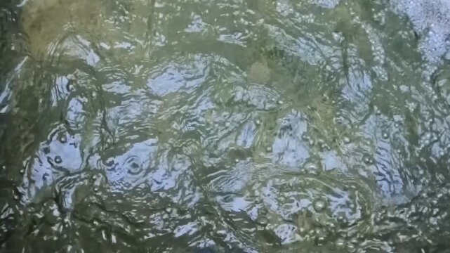 Vertical 1080p 240fps ultra slow motion video of fountain water ripples close up. Abstract top down shot of concentric liquid waves, fluid motion and sun light reflections texture background