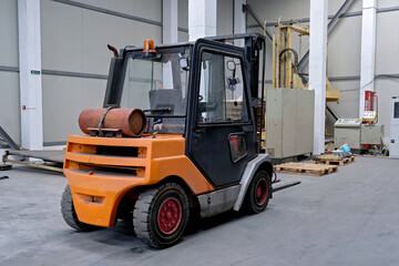 An orange and black industrial forklift truck with a gas cylinder mounted on the front parked in a warehouse. © Констянтин Батыльчук