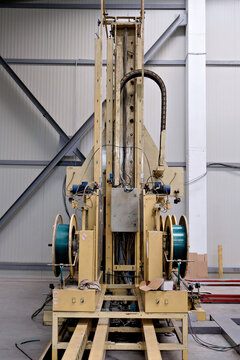A full view of an industrial vertical packaging machine equipped with two large spools of teal strapping band, columns, and automated mechanisms on a factory floor.