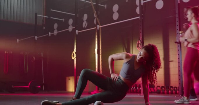 African American woman in sportswear lowering onto mat, rolling on foam roller at gym for mobility