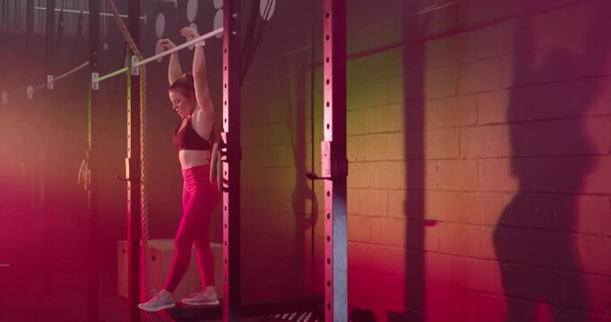 Woman stepping on gym box, pulling on pull-up bar, kipping, training in pink leggings, copy space