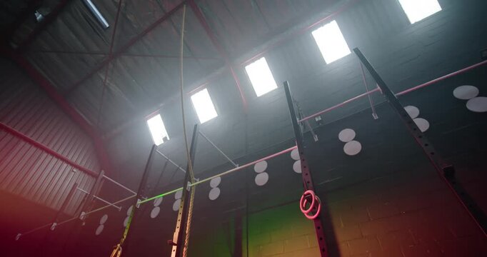 Camera is lowering, revealing pull-up rig with rings and rope in gym, showcasing colored lights