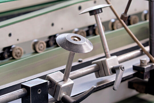 Detailed view of circular guide discs mounted on a steel rail with manual adjustment levers on a manufacturing machine line.